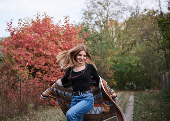 Full-length portrait of pretty blond woman jumping running in autumn park forest woods. Young girl, wearing blue jeans and colorful cardigan, posing on natural background, having fun. Hippie style.