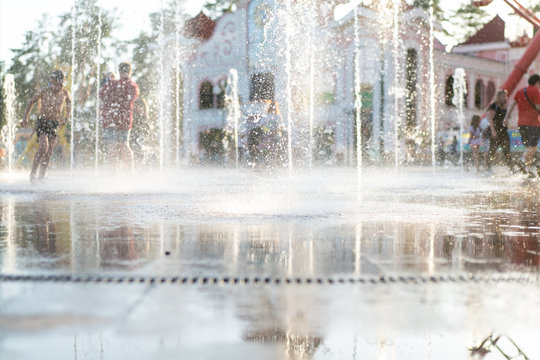 Unrecognizable Happy Kids Have Fun Playing In City Dry Water Fountain On Hot Summer Day