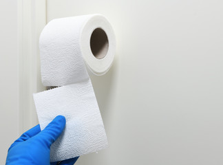 A man in rubber gloves tears off a piece of toilet paper roll of toilet paper on a white background. Disinfection in public places, the fight against the virus, coronavirus.