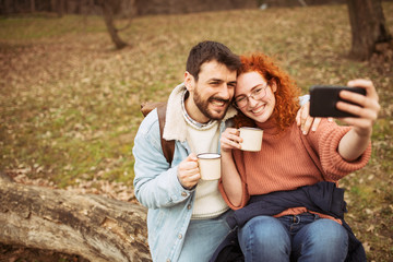 Young couple using modern technology. Smiling couple drinking coffee in the park. the couple use a nice sunny spring day to party in the park.