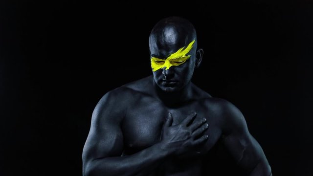 Man sports fan and bodybuilder athlete with yellow color on face art and black body paint. Colorful portrait of the guy with bodyart. Slow motion.