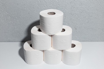 Close-up of toilet paper rolls on white table, background of textured wall grey of color.