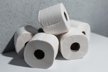 Close-up of toilet paper rolls on white table, background of textured wall grey of color.