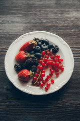 Strawberries, currants and blueberries on a dark background. Plate with wild berries.