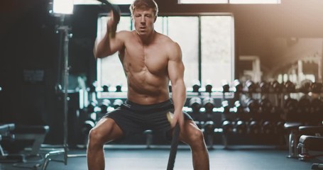 Attractive muscular man working out in the gym using battle ropes with high intensity, determined fitness man achieving his goals - Powered by Adobe