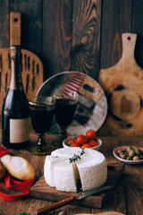  Composition with cheese and wine with cherry tomatoes. A large smooth round curd cheese on a plate.