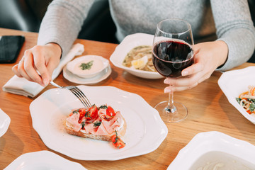 Restaurant dish on the menu with wine. The girl is eating bruschetta with bacon and tomato.