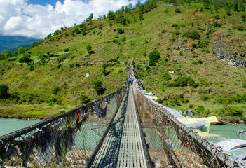 Fototapeta na wymiar The longest suspension bridge in Bhutan anchored at the bank of Tsang river projecting horizontally to the other bank and adorned with thousands of the Bhutanese prayer flags