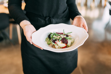  Fresh salad on a white plate. The waiter carries the dish in the restaurant.
