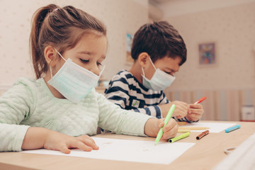 Cute children boy and girl in medical mask is sitting at home in quarantine. Сhildren play constructor after disinfection hands. Entertainment for the children during quarantine. Self isolation.      