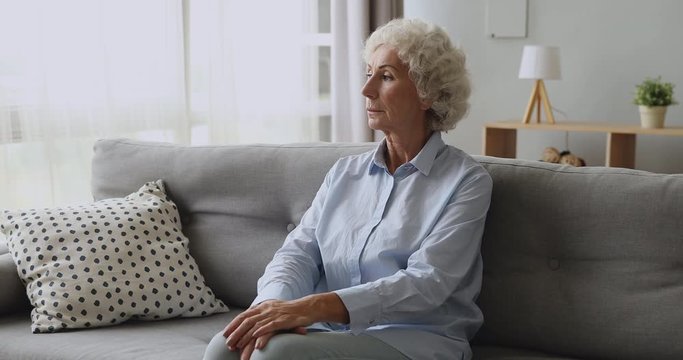 Unhappy middle aged mature pensive woman sitting on sofa at home thinking of problems or family troubles. Upset lost in thoughts older sad lady feeling lonely, suffering from depression alone.