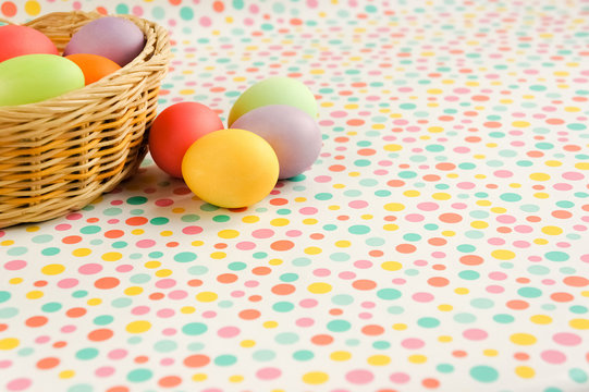 Multi-colored Easter eggs in a wicker basket on a polka dot background.