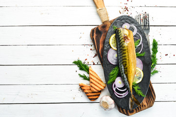 Smoked fish mackerel with onion and lemon on a black plate. Top view. Free space for your text....