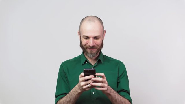 Handsome happy bearded man using mobile phone over white background. People sincere emotions, lifestyle concept. Looking surprised using cell phone.