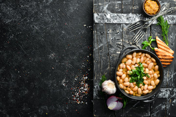 Boiled beans with parsley in a black plate. Top view. Free space for your text. Rustic style.
