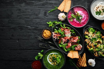 Background food and dishes. Salads, snacks and soups on black background. Top view.