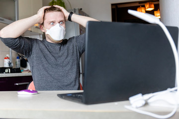 Fototapeta na wymiar young man in protective medical mask with horror watching the news on a laptop, home quarantine during a pandemic
