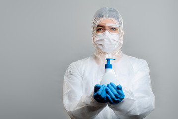 Medical worker in protective suit, glasses, gloves with liquid soap in hands isolated on gray background in studio.