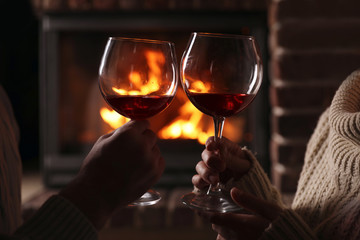 Lovely couple with glasses of wine near fireplace at home, closeup. Winter vacation