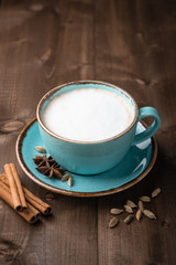 Masala tea in a ceramic cup with cardamom, star anise, cinnamon and ginger on a wooden background. Antiviral drink for immunity. 