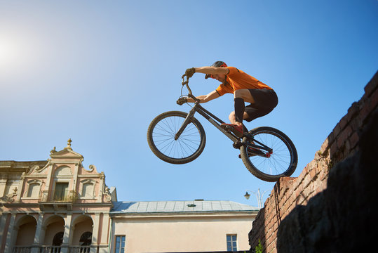 View from below sporty man on a black sport bike in motion performing a somersault. Bike with athlete standing on red bricks. Concept of rest.
