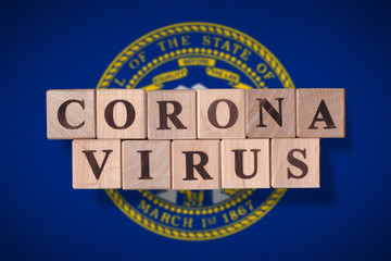 Flag of the state of Nebraska with wooden cubes spelling coronavirus on it. 2019 - 2020 Novel...