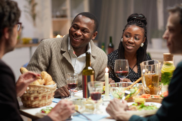 Young African couple sitting at holiday table and talking to their friends during dinner at home