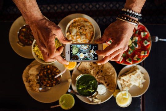 man's hands taking photo with a smartphone of indian food on the table, top view