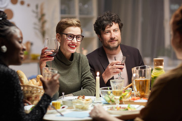 Young couple smiling and drinking wine while talking to the friends they celebrating the holiday during dinner at the table