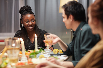 Young African woman smiling and talking to her friends while they sitting at the table and eating dinner