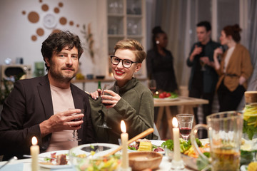 Portrait of young couple smiling at camera while sitting at the table and drinking wine during the party