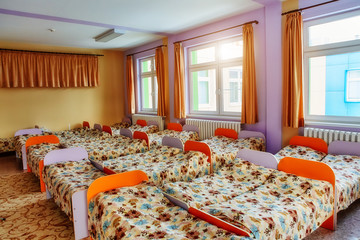 Many small beds with fresh linens in the kindergarten preschool empty bedroom interior for a comfortable afternoon sleep for children. Concept of quarantine in a children's institution