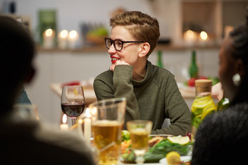 Young woman in eyeglasses smiling and talking to her friends at the holiday dinner at home