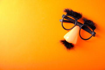 Overhead glasses, nose and mustache for April 1, April Fool's Day, on orange background - obrazy, fototapety, plakaty
