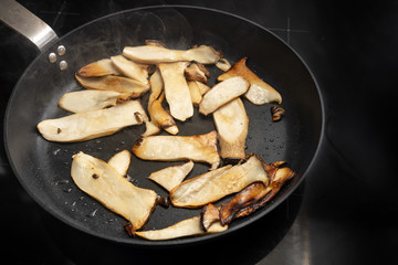 King oyster mushrooms, Pleurotus eryngii, are roasted in a black cooking pan on the stove, copy space