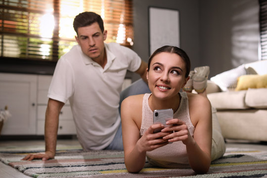 Distrustful man peering into girlfriend's smartphone at home. Jealousy in relationship