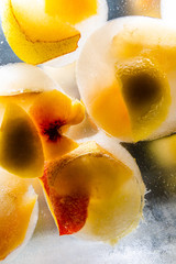 frozen peach, lemon and pear in water on transparent surface with glowing background