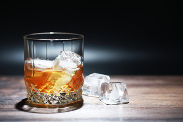A glass of strong alcoholic drink with ice on a wooden bar counter. Whiskey with ice cubes. Glass with a chilled drink.