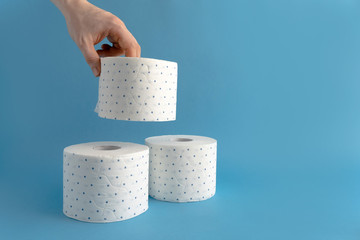 A male hand takes a roll of white toilet paper in a blue dot. Blue background. Place for text. Lack of toilet paper