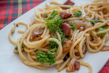 The dish of spaghetti with parsley and sausage bacon served on the red tartan table in the restaurant. 