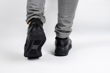 Girl's legs in gray jeans and black spring sports shoes on a light background, the girl seems to be walking and showing beautiful leather shoes. Rear view