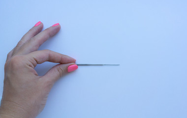 Woman's hand with pink manicure picking up the steel needle on white background. Concept of felting creative hobby.