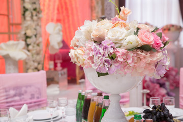 wedding table  . Large vase with beautiful roses stands on rich served dinner table .Wedding flower composition for guest . Beautiful pink and white flowers on table in wedding day .