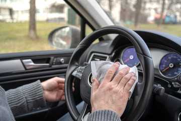 Man cleaning steering wheel of a car using antivirus antibacterial wet wipe (napkin) for protect himself from bacteria and virus.