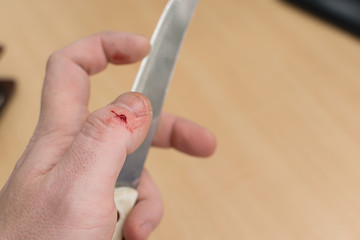 a clot of a drop of blood on the finger of the hand that holds a sharp knife