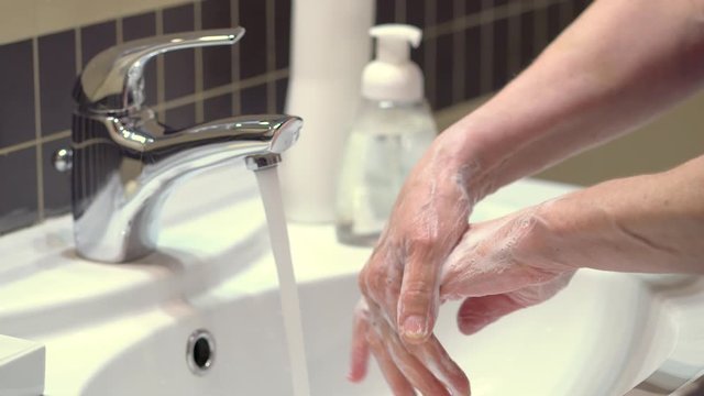 Hand hygiene. Protection against microbes and coronoviruses. The process of soaping the hands. Vigorous rubbing of the foam, followed by rinsing with water from the tap. Side view.