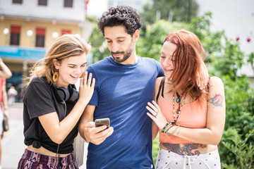 Naklejka premium three friends looking at their cell phones while smiling on the street