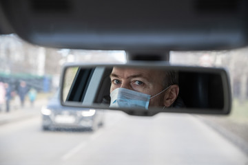 Reflection of face of middle aged man in the medical mask for protect himself from bacteria and virus while driving a car in the car rear view mirror. Coronavirus. Pandemic