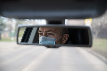 Reflection of face of middle aged man in the medical mask for protect himself from bacteria and virus while driving a car in the car rear view mirror. Coronavirus. Pandemic