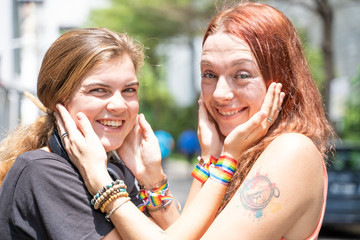 Couple of women caressing each other's faces while smiling and wearing a lgtb flag bracelet